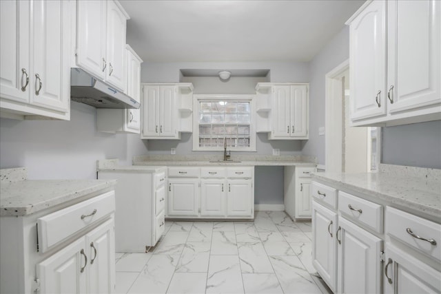 kitchen featuring light stone counters, white cabinetry, and sink