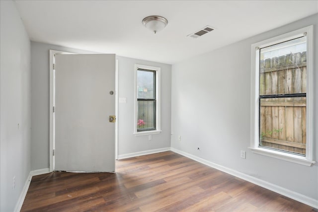 empty room with a wealth of natural light and dark hardwood / wood-style flooring