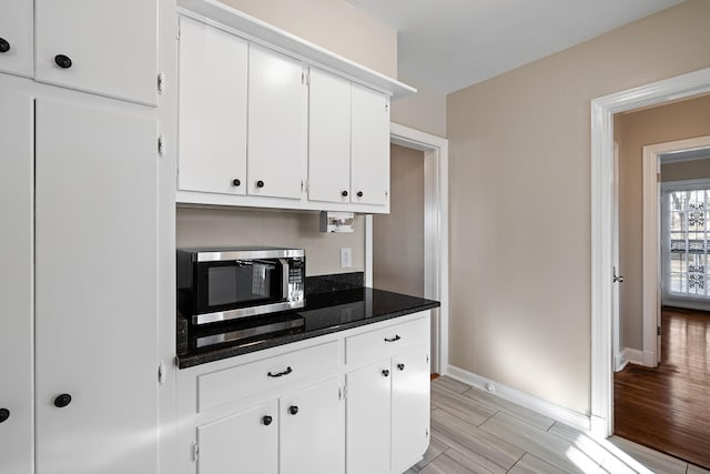 kitchen with light wood-type flooring, white cabinetry, and dark stone countertops