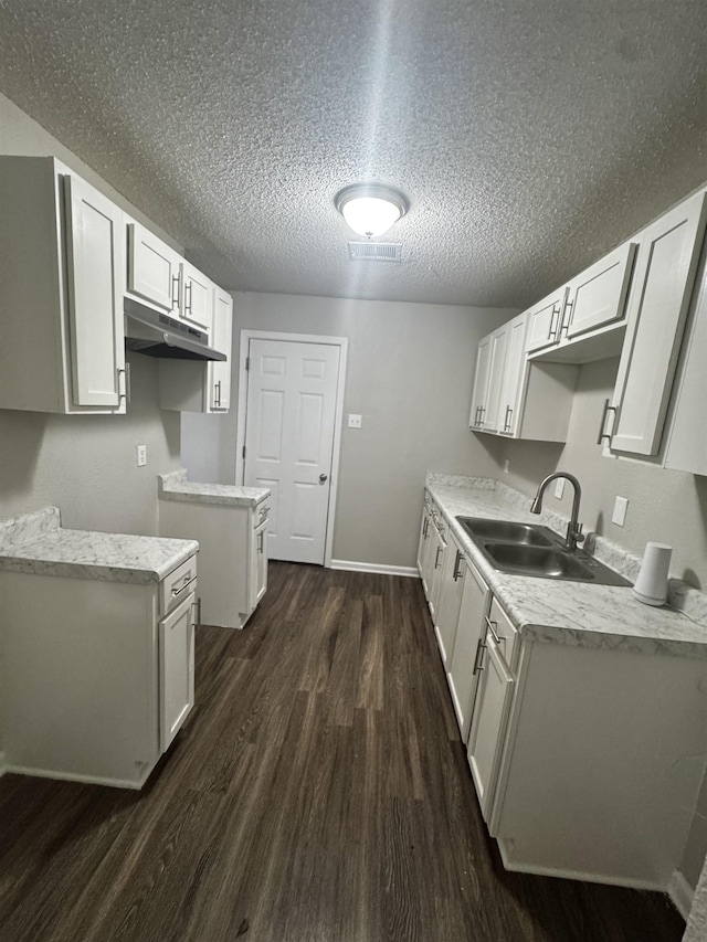 kitchen with a textured ceiling, dark hardwood / wood-style flooring, white cabinetry, and sink