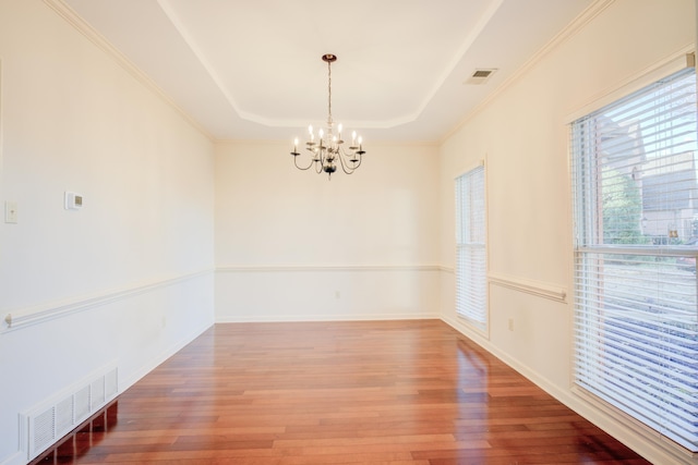 spare room featuring hardwood / wood-style floors, a notable chandelier, a raised ceiling, and ornamental molding