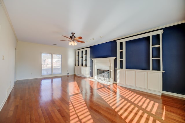 unfurnished living room featuring hardwood / wood-style floors, ceiling fan, built in features, and ornamental molding