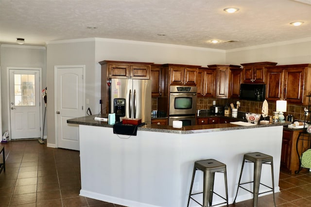 kitchen with appliances with stainless steel finishes, tasteful backsplash, dark tile patterned floors, and a kitchen breakfast bar