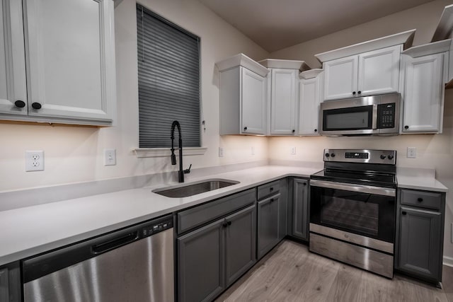 kitchen featuring gray cabinetry, sink, light hardwood / wood-style floors, white cabinets, and appliances with stainless steel finishes