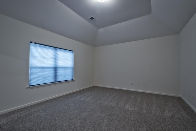 spare room featuring dark colored carpet and vaulted ceiling