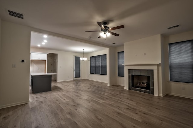 unfurnished living room featuring a tile fireplace, hardwood / wood-style floors, and ceiling fan with notable chandelier