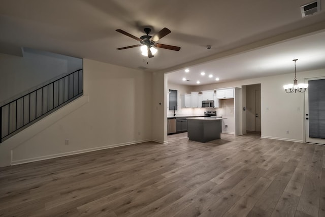 unfurnished living room with sink, ceiling fan with notable chandelier, and hardwood / wood-style flooring