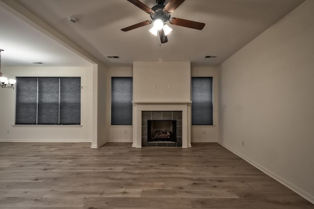 unfurnished living room featuring a tile fireplace, wood-type flooring, and ceiling fan with notable chandelier