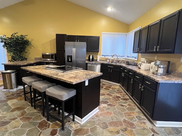 kitchen featuring light stone countertops, appliances with stainless steel finishes, sink, a center island, and a breakfast bar area