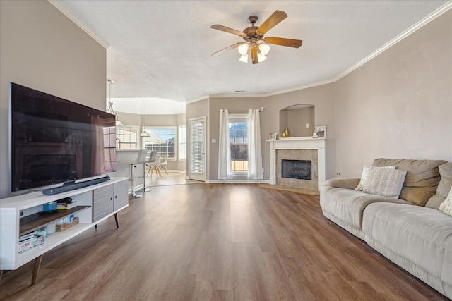 living room featuring hardwood / wood-style floors, crown molding, ceiling fan, a textured ceiling, and a tiled fireplace