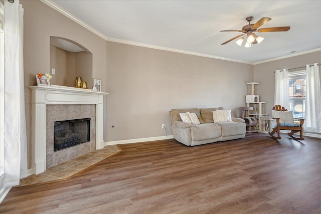 living room with a tiled fireplace, ceiling fan, crown molding, and wood-type flooring