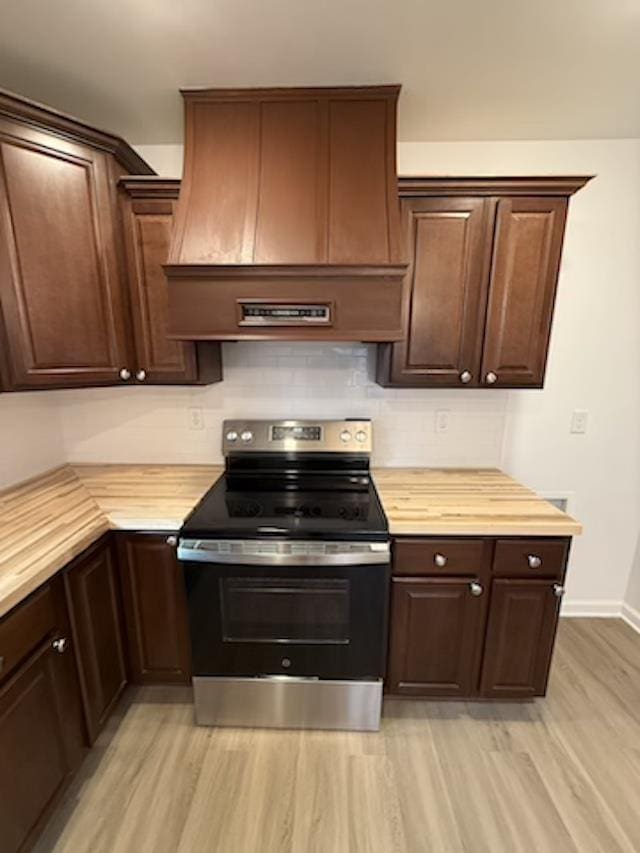 kitchen with dark brown cabinetry, premium range hood, stainless steel range with electric stovetop, and light hardwood / wood-style floors