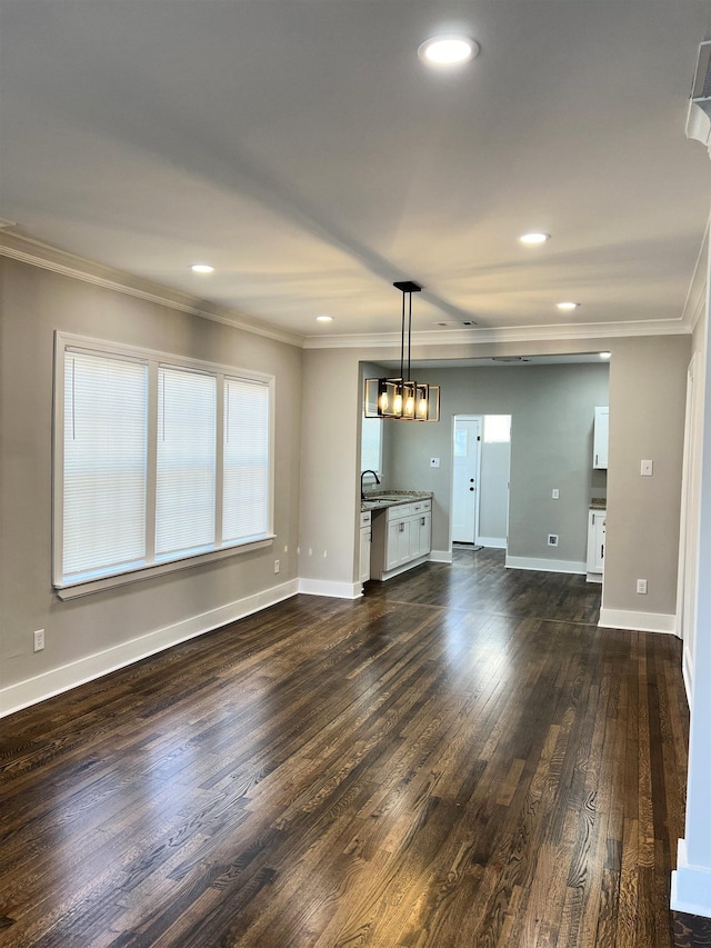 unfurnished living room featuring crown molding, sink, dark wood-type flooring, and a notable chandelier