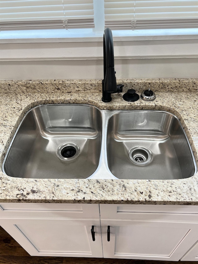 room details with white cabinetry, light stone countertops, and sink