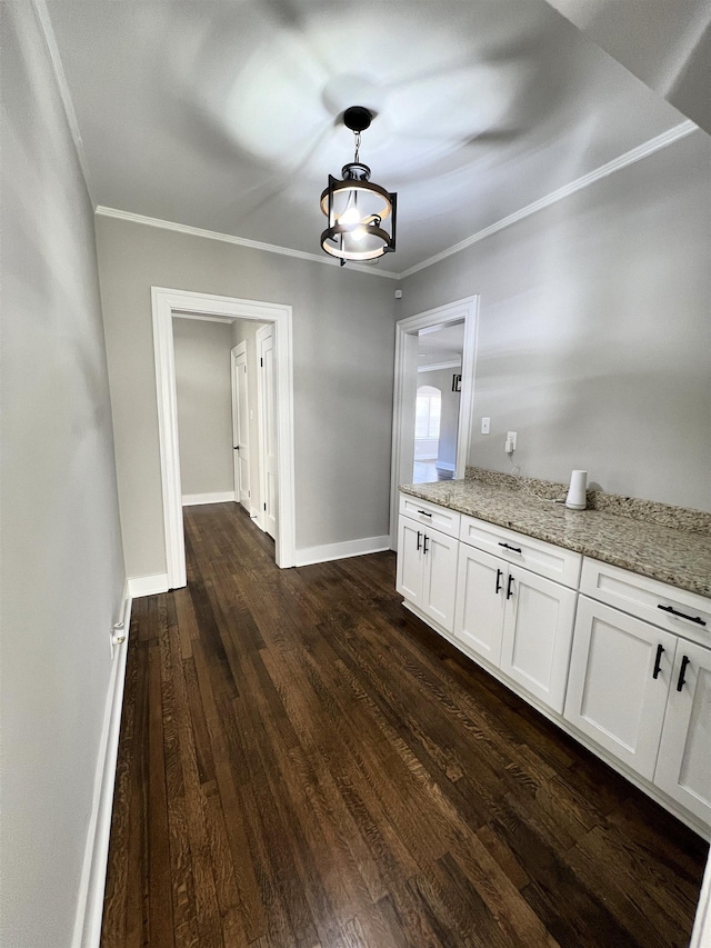 interior space featuring white cabinetry, hanging light fixtures, light stone counters, dark hardwood / wood-style flooring, and ornamental molding