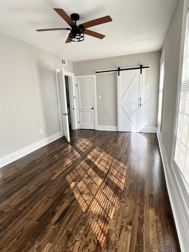 unfurnished bedroom with ceiling fan, a barn door, and dark hardwood / wood-style flooring