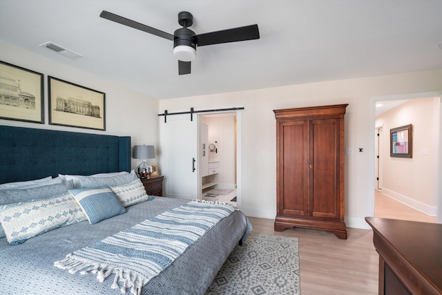 bedroom featuring ceiling fan, light hardwood / wood-style floors, a barn door, and ensuite bathroom