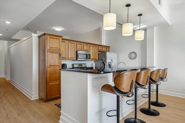 kitchen with hanging light fixtures, appliances with stainless steel finishes, tasteful backsplash, light hardwood / wood-style floors, and kitchen peninsula