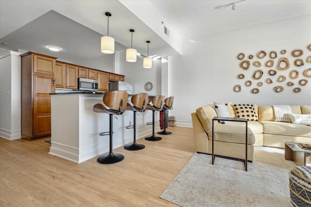 kitchen featuring a kitchen breakfast bar, light hardwood / wood-style flooring, hanging light fixtures, and appliances with stainless steel finishes