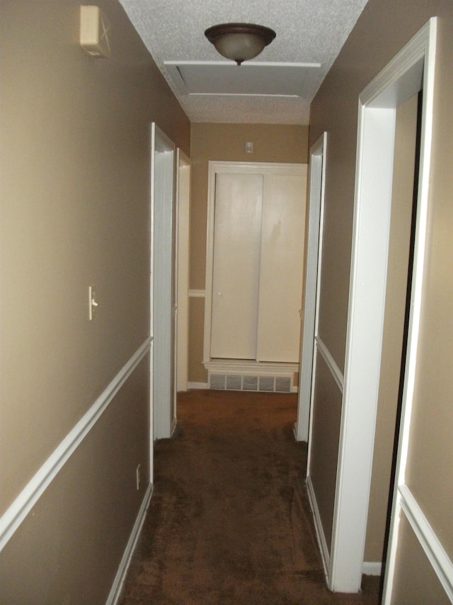 corridor featuring dark colored carpet and a textured ceiling