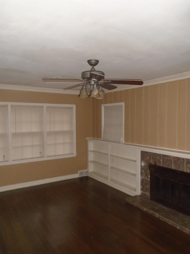 unfurnished living room featuring a tile fireplace, built in shelves, crown molding, and dark wood-type flooring