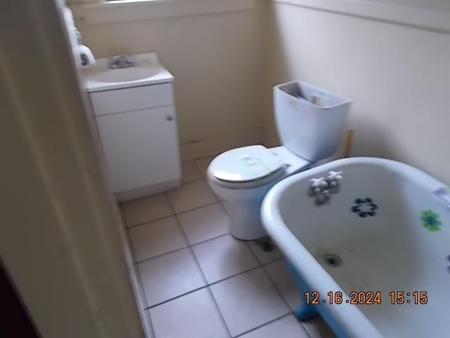 bathroom featuring tile patterned flooring, a bath, vanity, and toilet