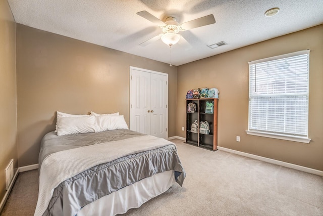 carpeted bedroom with ceiling fan, a closet, and a textured ceiling