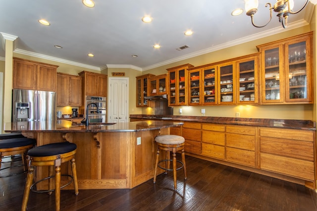 kitchen with a center island with sink, ornamental molding, stainless steel appliances, and dark wood-type flooring