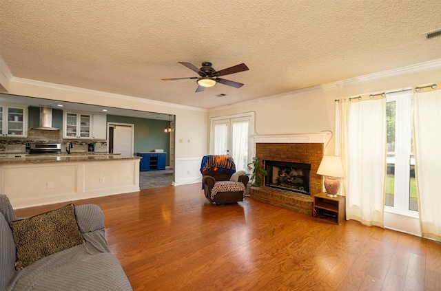 living room featuring ornamental molding, wood-type flooring, a brick fireplace, and a textured ceiling