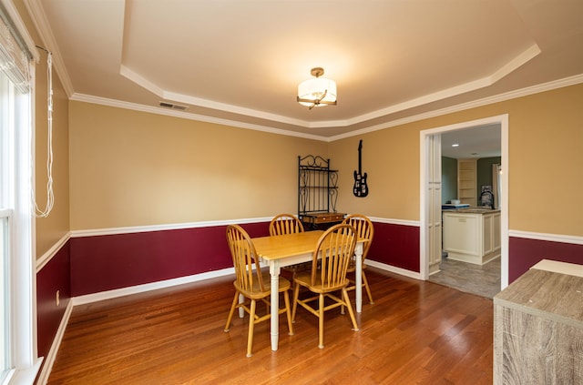 dining area featuring ornamental molding, wood-type flooring, and a tray ceiling