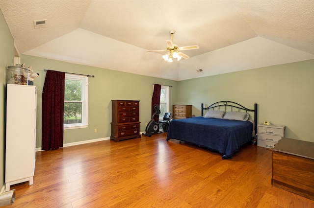 bedroom featuring multiple windows, vaulted ceiling, hardwood / wood-style floors, and a tray ceiling