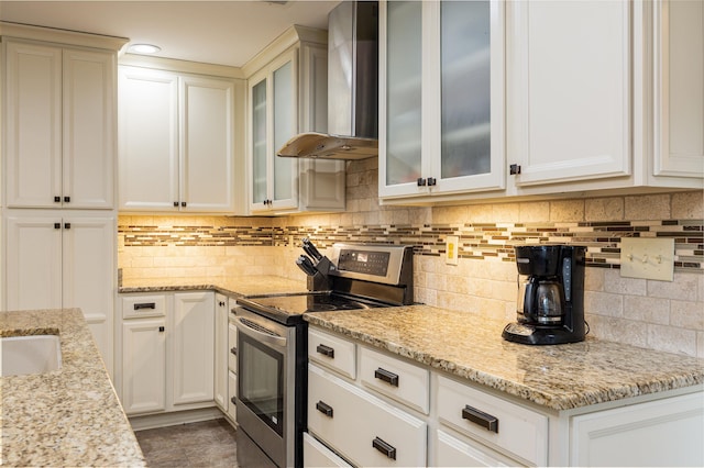 kitchen featuring tasteful backsplash, white cabinets, electric range, light stone counters, and wall chimney exhaust hood