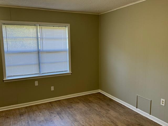 unfurnished room with wood-type flooring, a textured ceiling, and ornamental molding