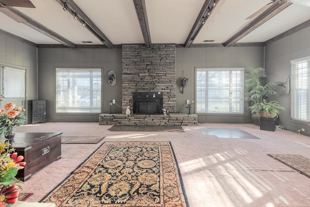 carpeted living room with beam ceiling, rail lighting, and a stone fireplace