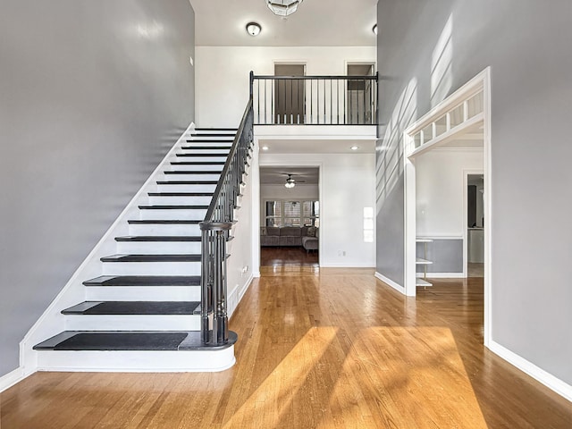 stairs with ceiling fan, wood-type flooring, and a high ceiling