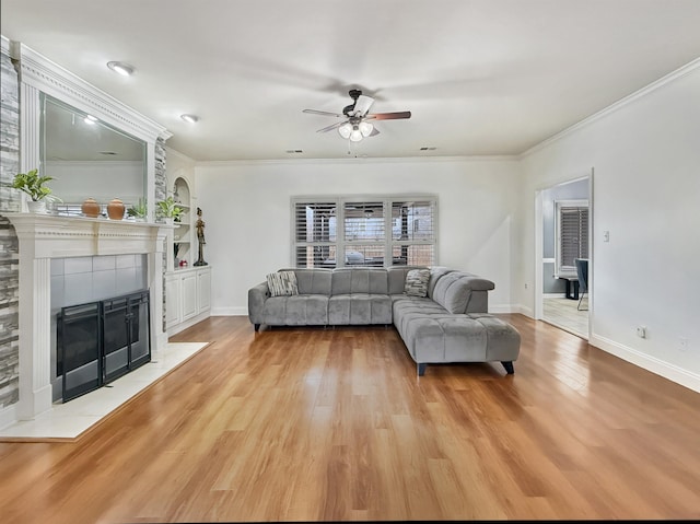 living room with ceiling fan, ornamental molding, a fireplace, and light hardwood / wood-style flooring