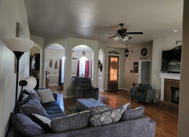 living room with a fireplace, ceiling fan, and dark wood-type flooring