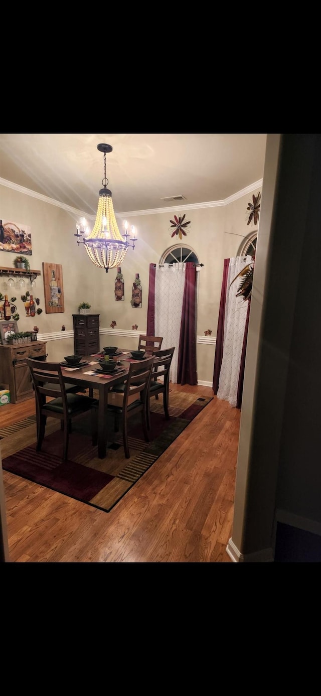 dining area featuring crown molding, wood-type flooring, and an inviting chandelier