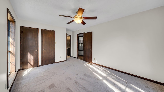 unfurnished bedroom featuring ceiling fan, light carpet, and two closets