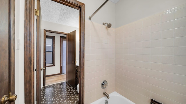 bathroom featuring a textured ceiling and tiled shower / bath