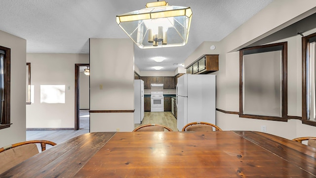 unfurnished dining area with light hardwood / wood-style flooring, a textured ceiling, and an inviting chandelier