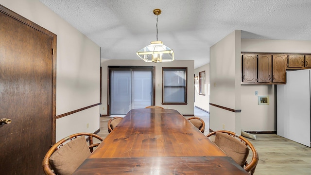 dining area with light hardwood / wood-style floors, a textured ceiling, and an inviting chandelier