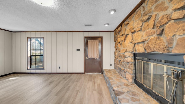 entryway with a textured ceiling, light hardwood / wood-style floors, crown molding, and a fireplace