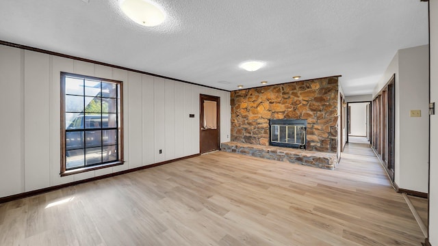 unfurnished living room with a textured ceiling, crown molding, light wood-type flooring, and a fireplace