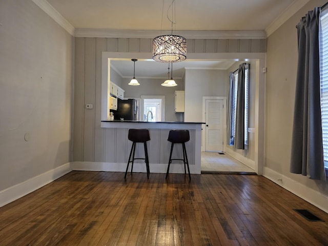 kitchen featuring a peninsula, visible vents, white cabinetry, ornamental molding, and freestanding refrigerator