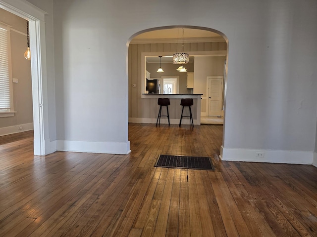 unfurnished dining area featuring dark wood-style floors, arched walkways, and baseboards