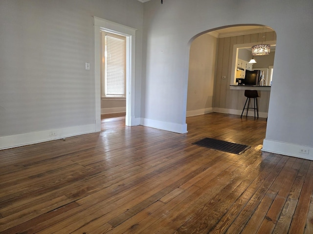 spare room with baseboards, visible vents, arched walkways, and dark wood finished floors