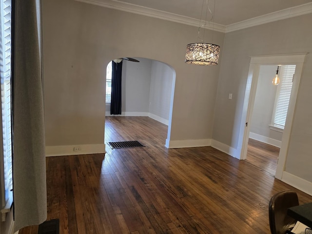 unfurnished dining area featuring arched walkways, dark wood-style flooring, visible vents, baseboards, and crown molding