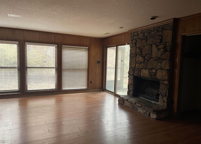 unfurnished living room with light wood-type flooring, a fireplace, wooden walls, and a textured ceiling