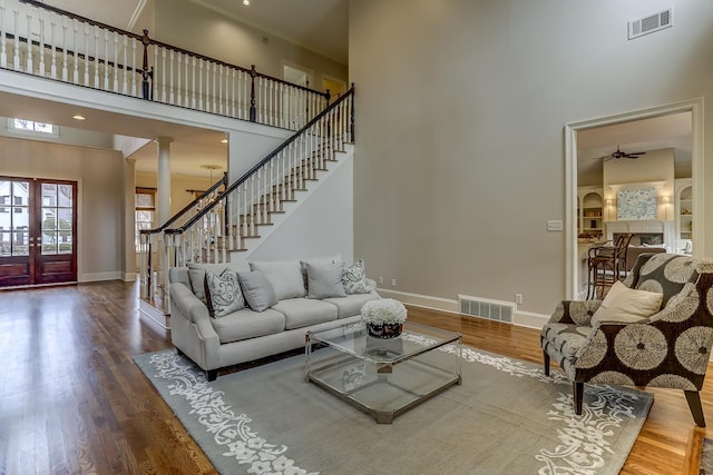 living room with a high ceiling, french doors, hardwood / wood-style flooring, ceiling fan, and decorative columns